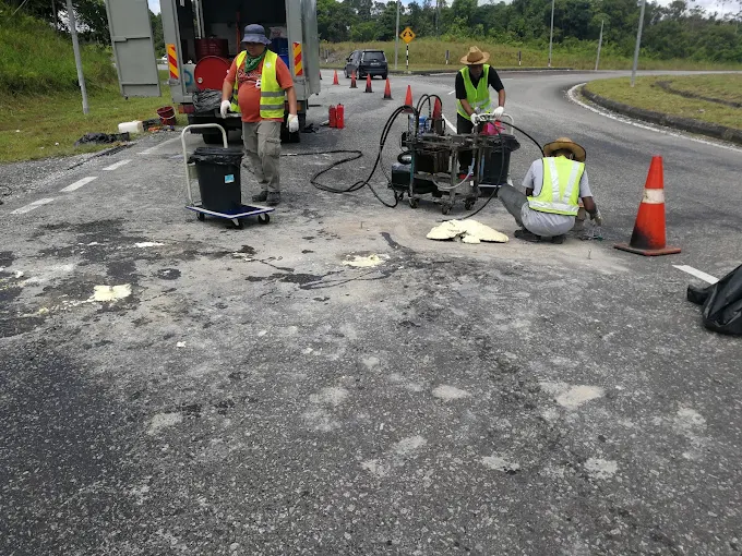 Geocon crew injecting polyurethane into a settled road pavement, with the injection rig and traffic cones on site